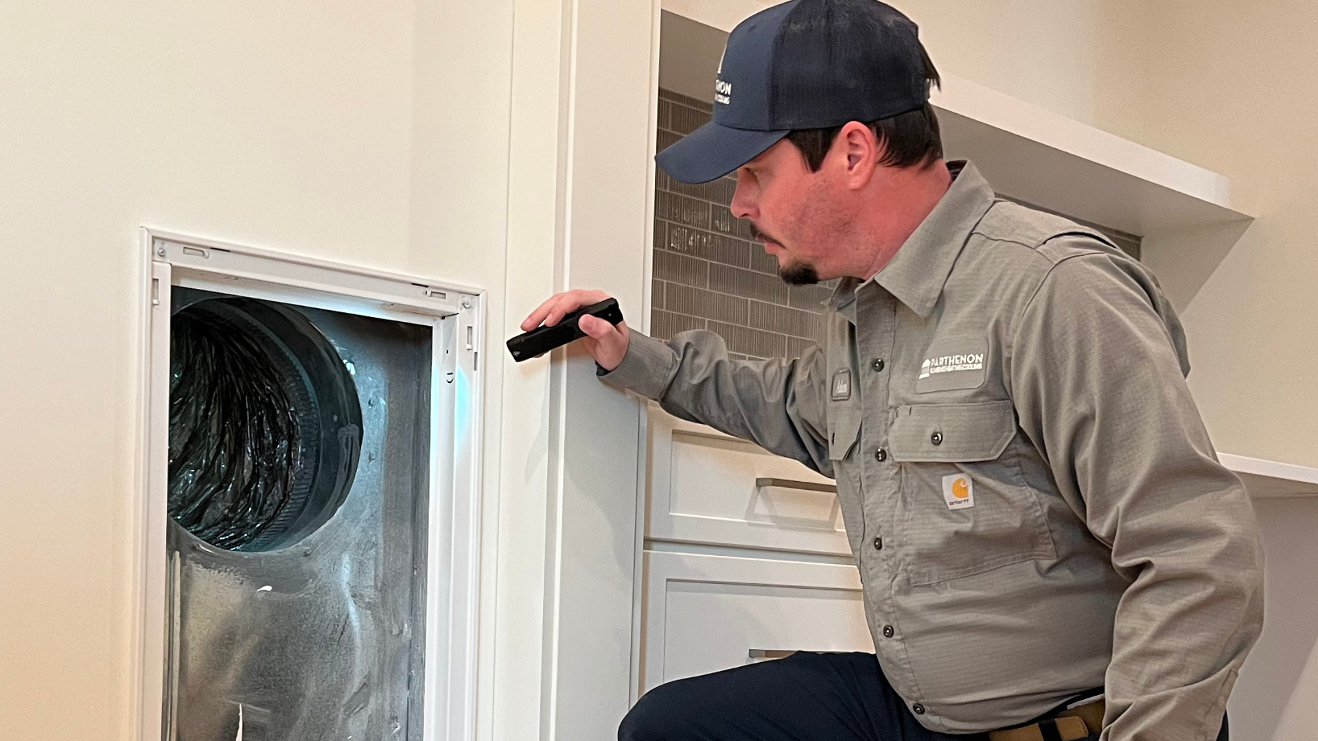 Technician inspecting a vent with a flashlight indoors.