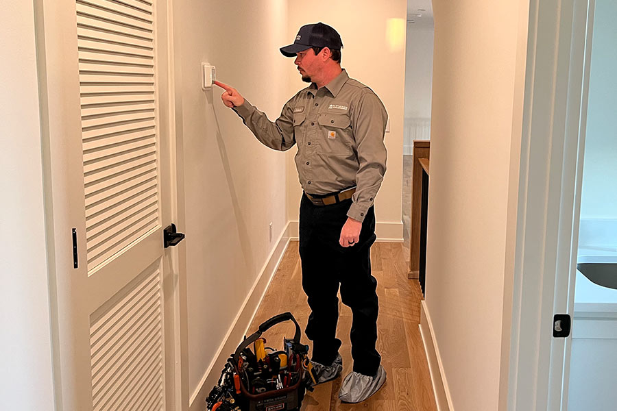 Technician adjusts thermostat in hallway with tool bag nearby
