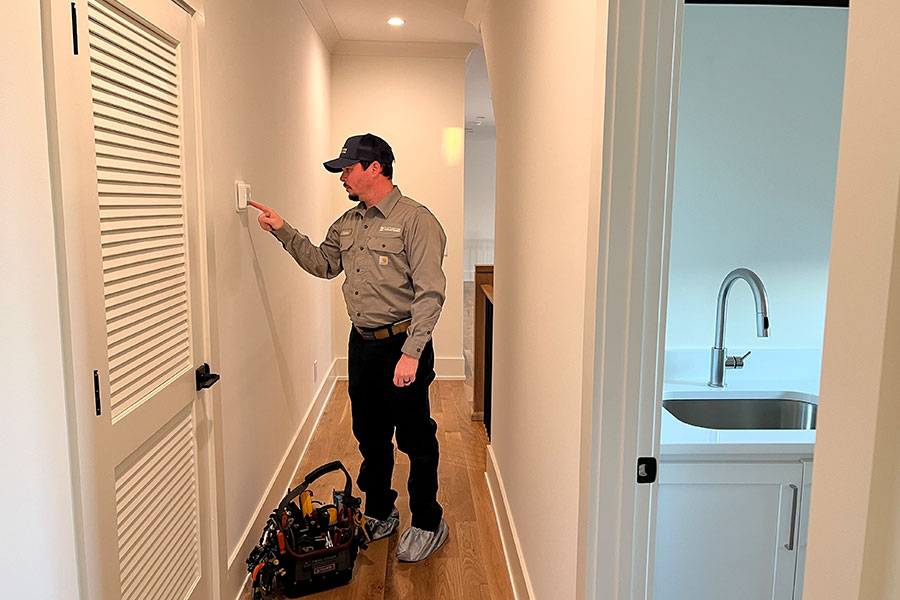 HVAC technician checking thermostat in a residential hallway