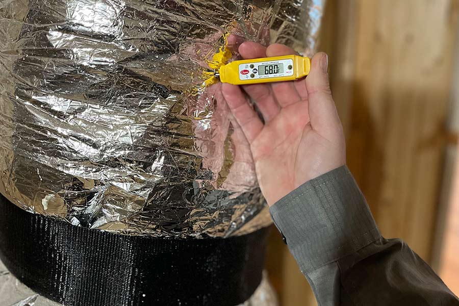 Thermometer reading duct temp during HVAC system check