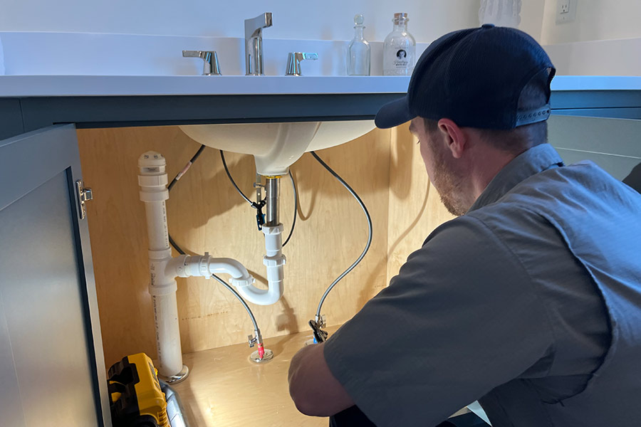Plumber checking pipes beneath bathroom vanity sink