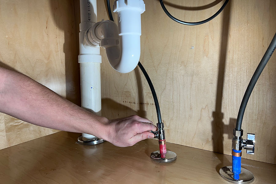 Hand tightening hot water line under bathroom sink