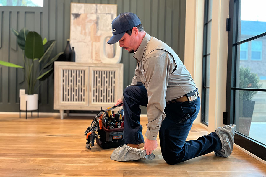 Technician kneeling to put on shoe covers in a home