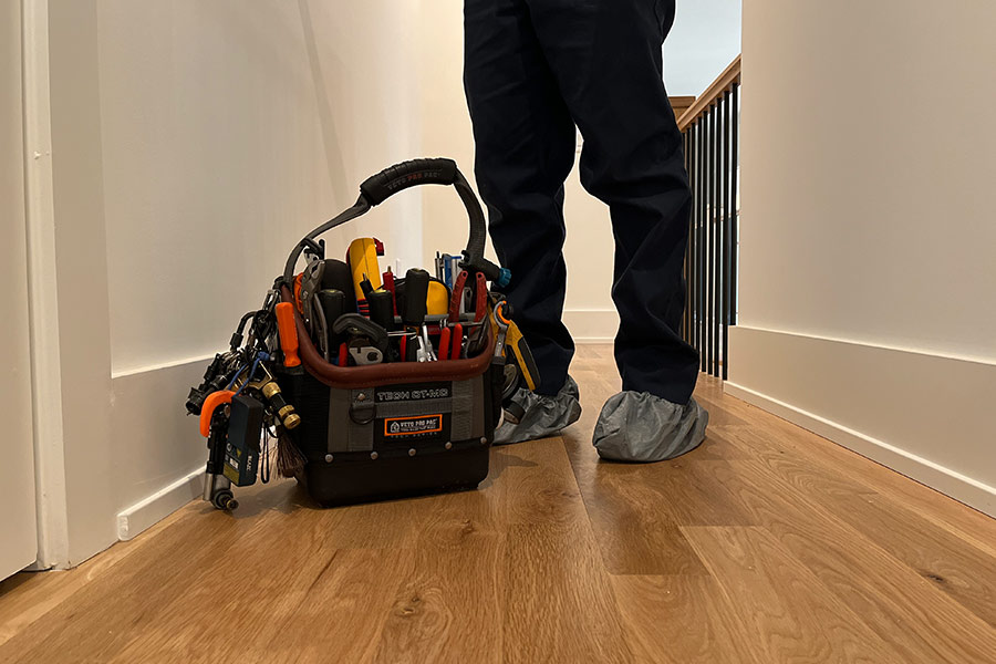 Technician in shoe covers standing next to tool bag indoors