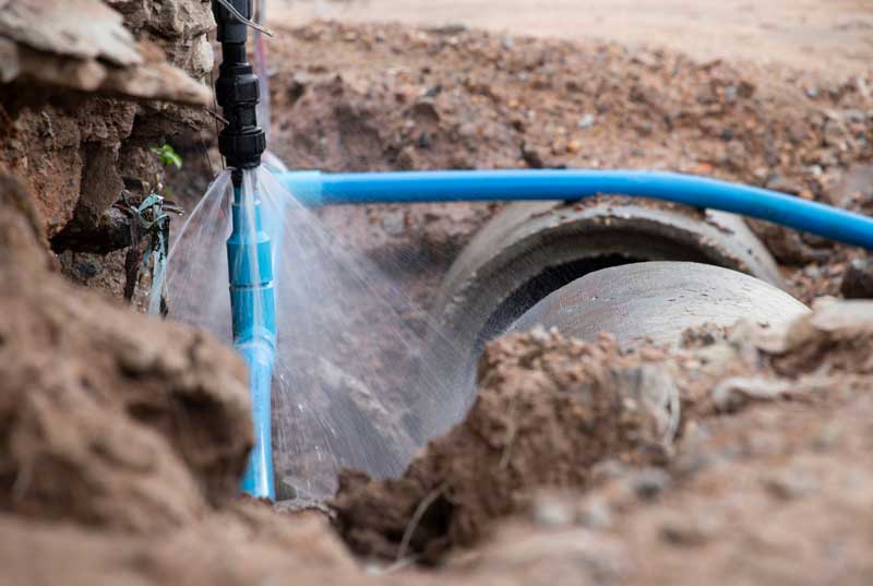 Broken blue water pipe spraying in a dirt excavation site