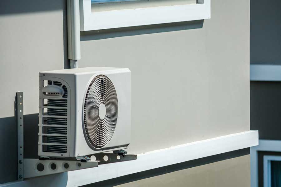 Outdoor wall-mounted AC unit under a window on brackets