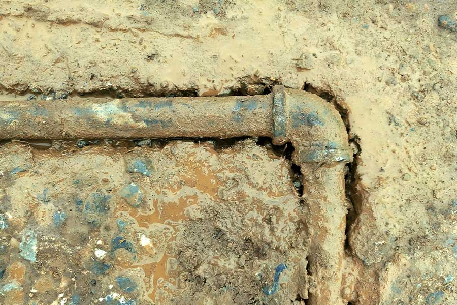 Rusty pipe joint buried in wet muddy soil