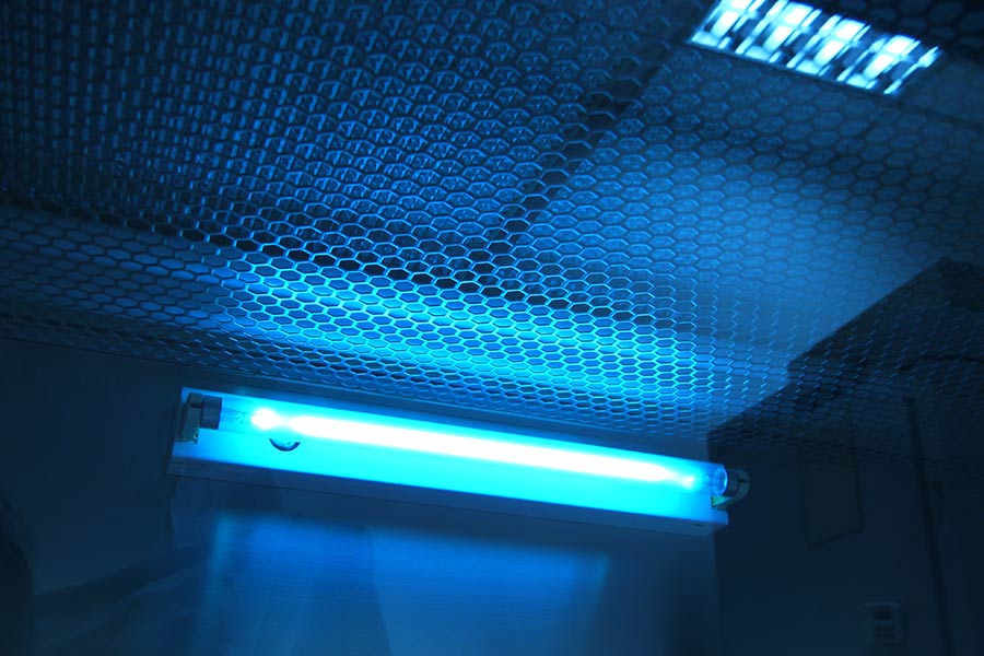 Blue UV light tube glowing behind mesh ceiling in a room