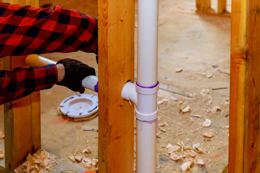 Person installing a white PVC pipe in a wooden frame