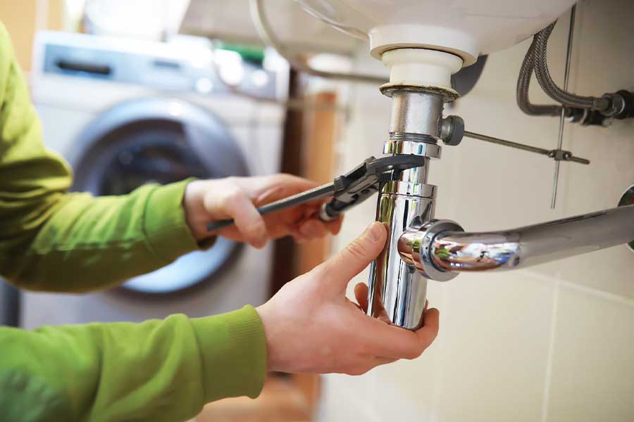 Person using a wrench to tighten a pipe under a sink
