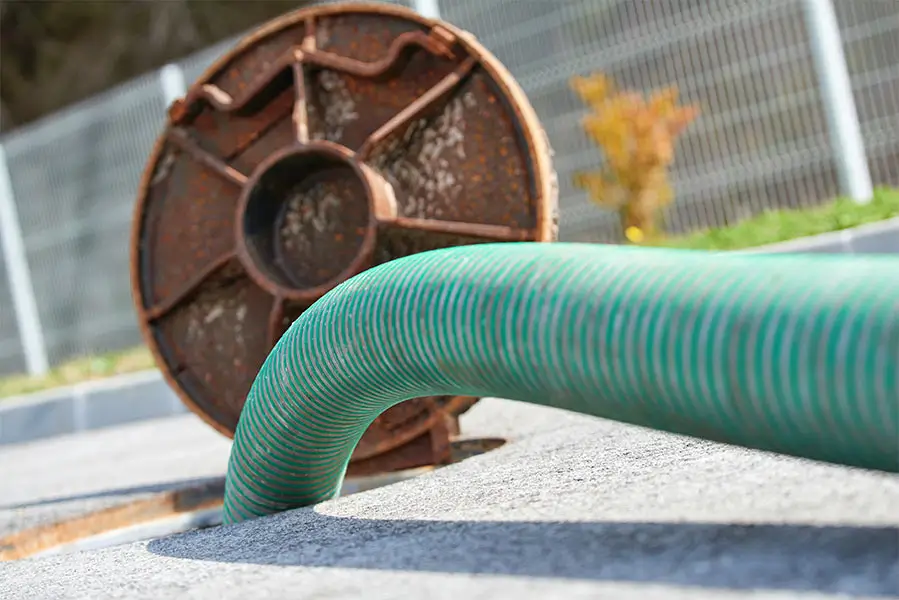 Green industrial hose inserted into an outdoor sewer opening