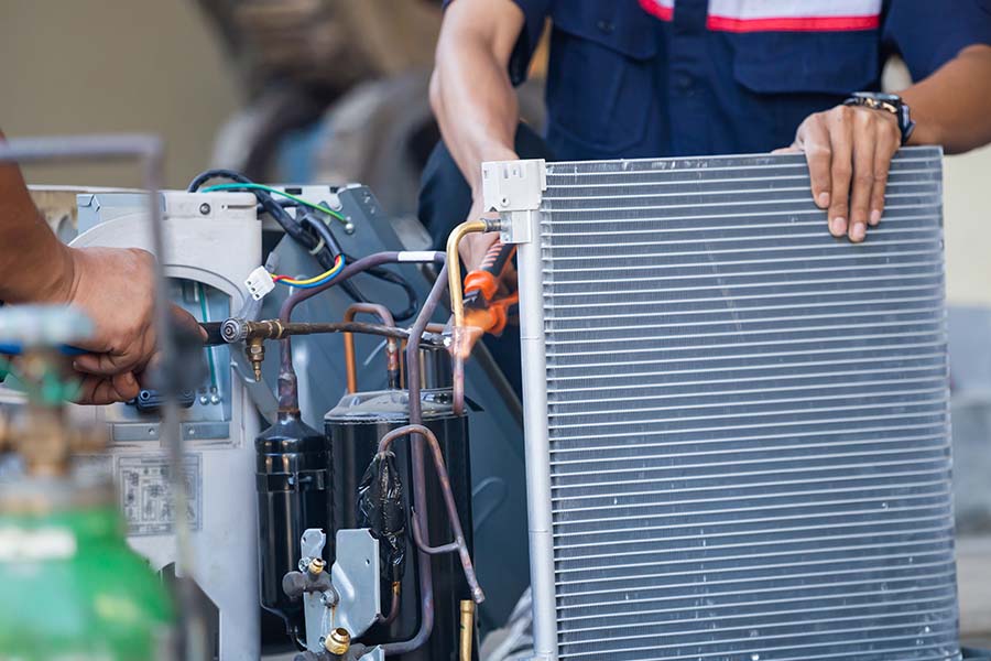 Technician servicing an HVAC unit with a coil and tools.