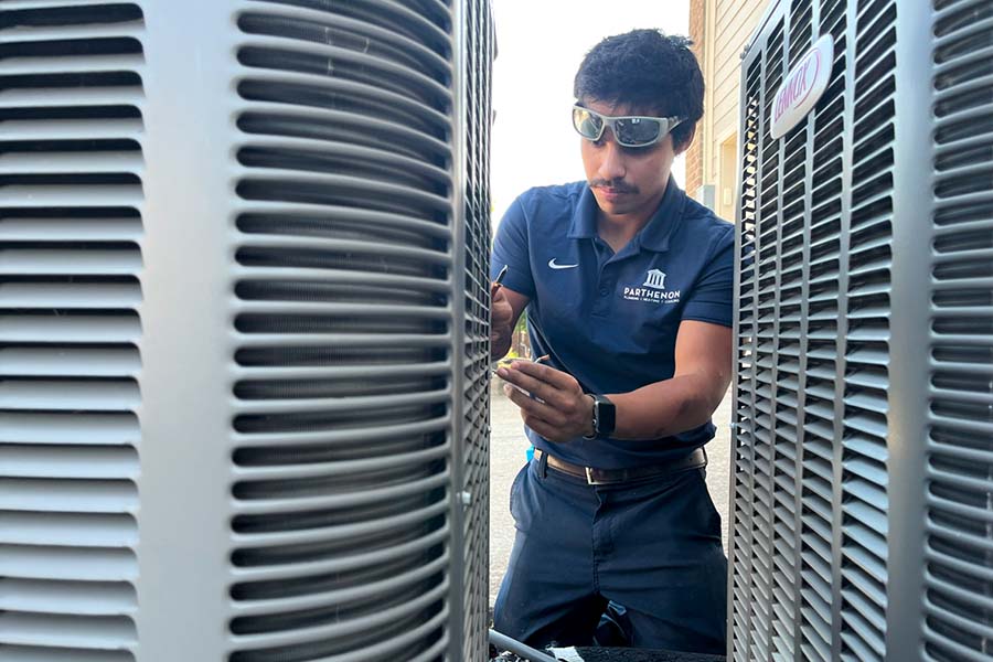 Technician working between outdoor HVAC units during a repair service